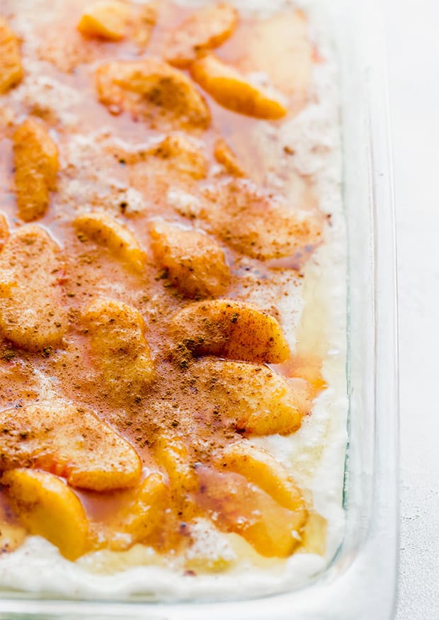 A close up photo of peach cobbler sprinkled with cinnamon, prior to going in the oven.