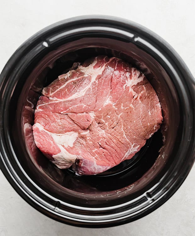 A slow cooker with a beef chuck roast in it, prior to cooking and making a Mississippi Pot Roast Recipe.