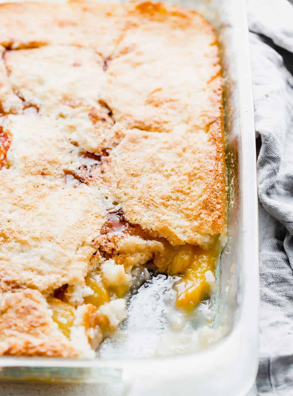 Easy Peach Cobbler baked in a glass pan with a portion of the cobbler scooped out of the pan.