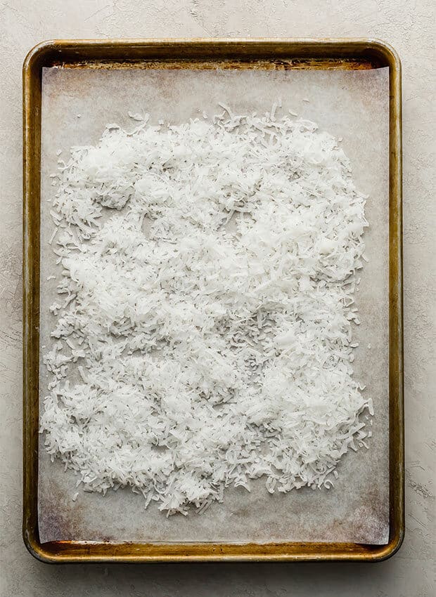 A baking sheet with shredded coconut on it, prior to baking and toasting the coconut.