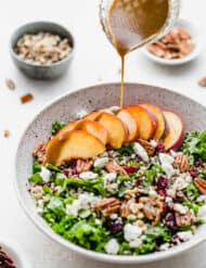 A balsamic dressing being drizzled over fresh peaches on a bed of kale and quinoa salad.