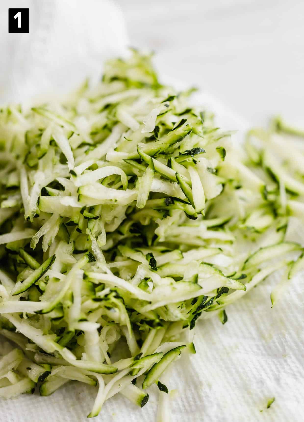 Shredded zucchini on a white paper towel.