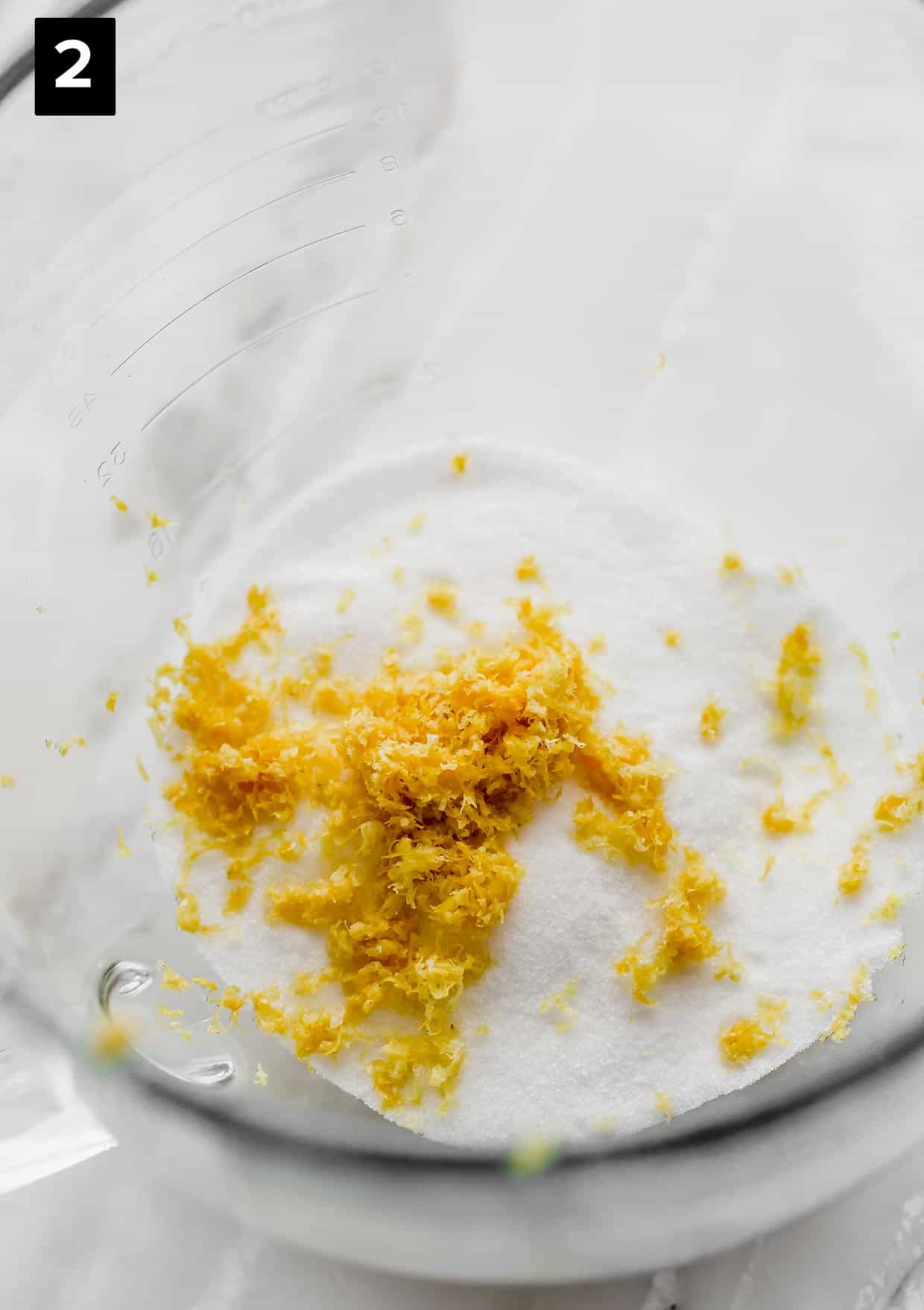 Sugar and lemon zest in a glass bowl, used to make a sour cream lemon zucchini loaf.
