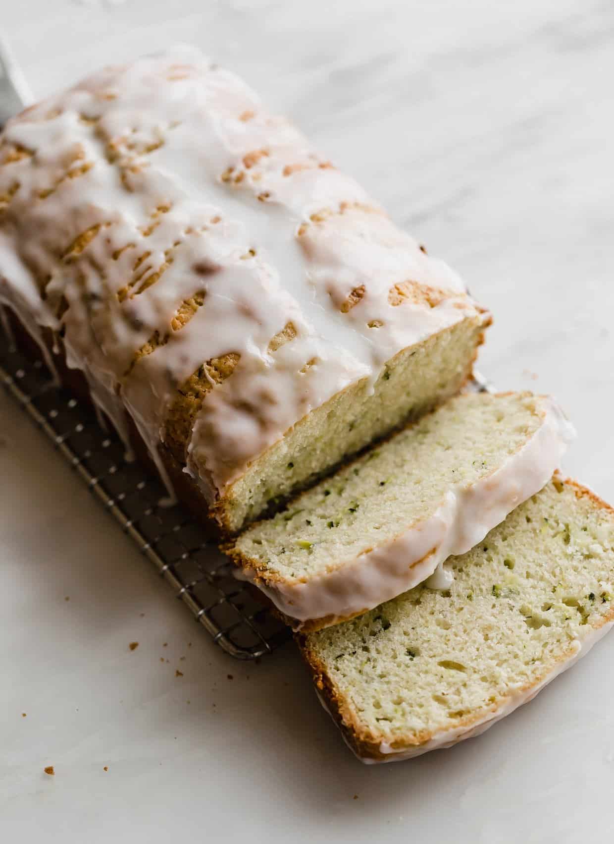 A loaf of glazed Lemon Zucchini Bread with sour cream, on a white marble background.