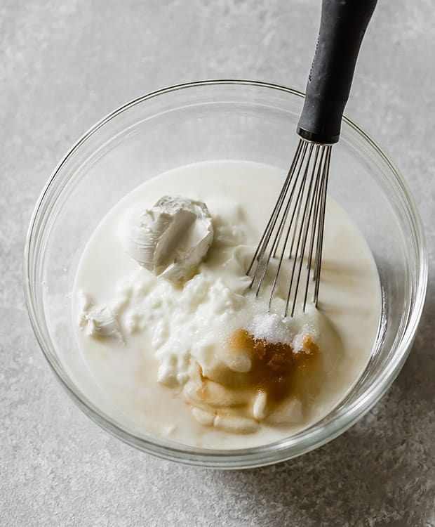 A glass bowl with the ingredients to make cookies and cream popsicles.