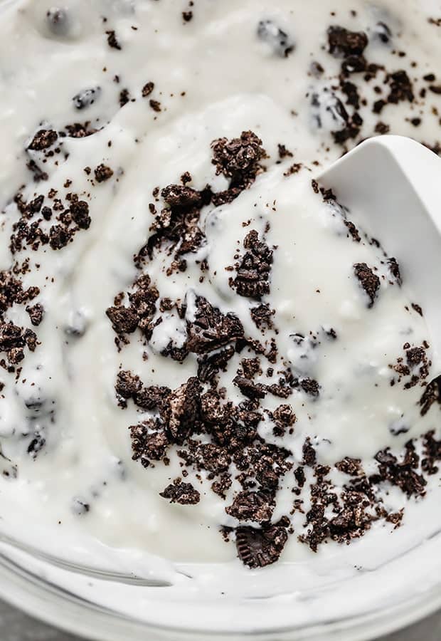 A close up photo of crushed Oreo's being mixed into cookies and cream popsicle mixture.