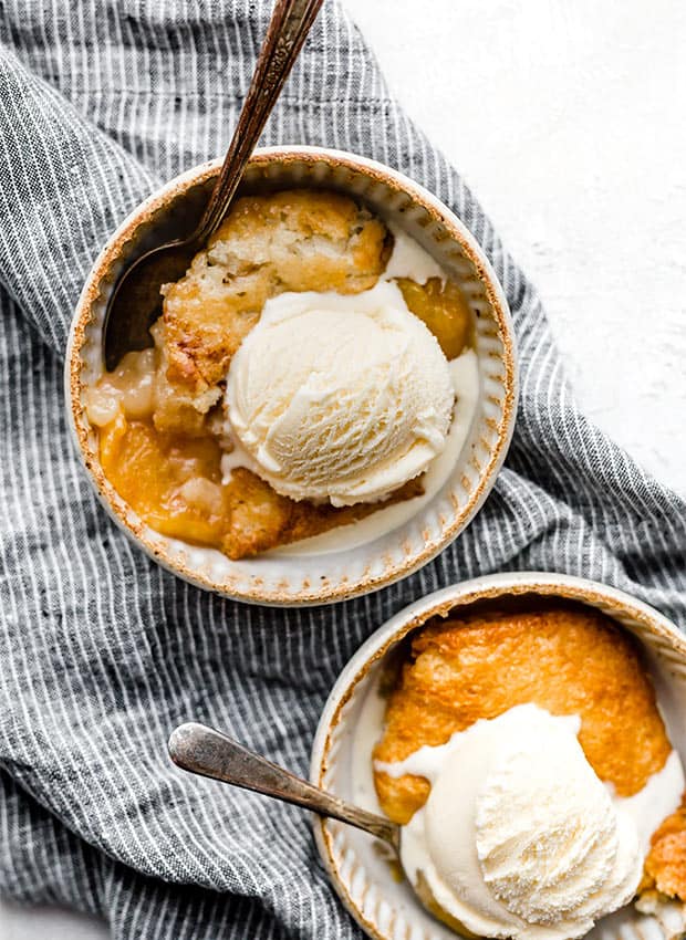 Two bowls with a serving a peach cobbler and vanilla ice cream.