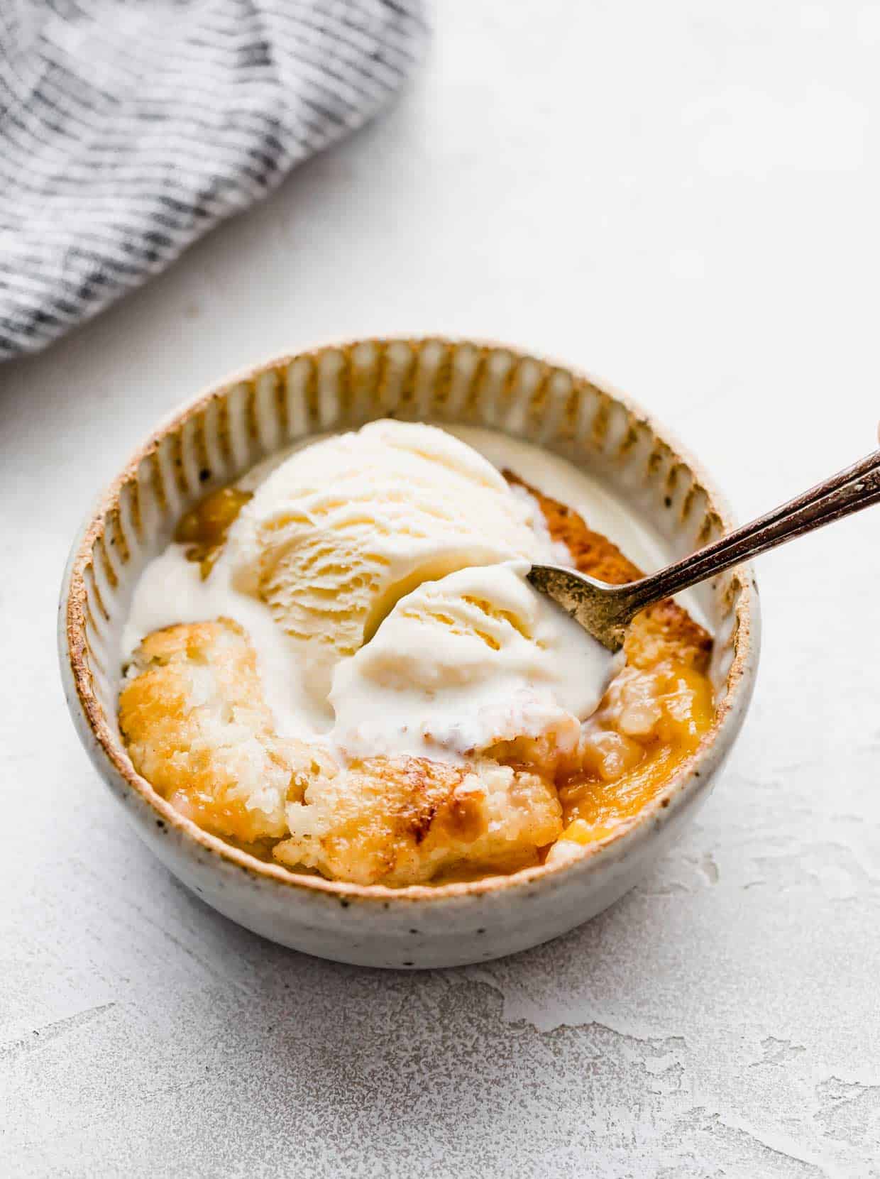 Old Fashioned Peach Cobbler in a bowl with vanilla ice cream overtop.