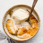 An old fashioned easy peach cobbler recipe, with a scoop of ice cream overtop and a spoon.