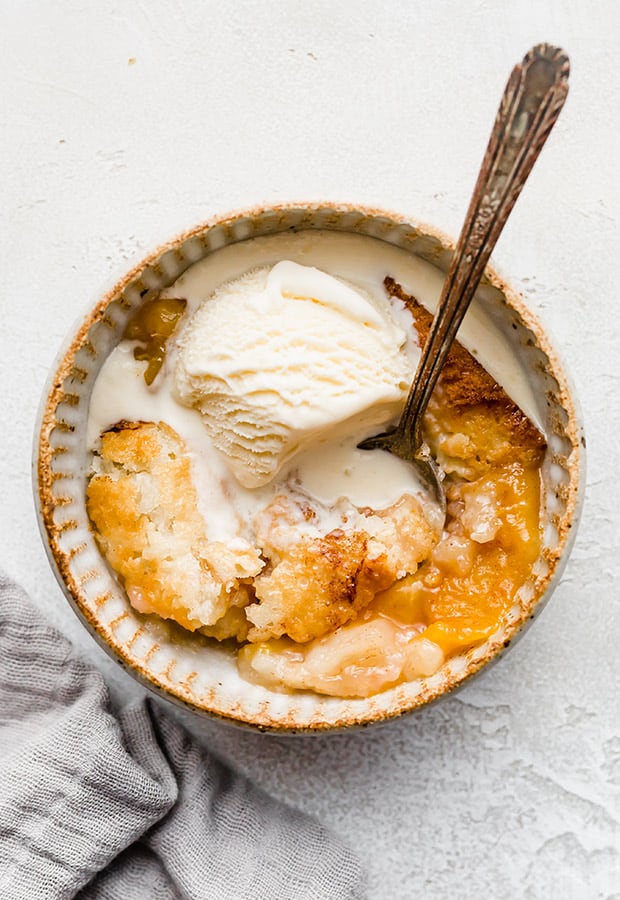 An old fashioned easy peach cobbler recipe, with a scoop of ice cream overtop and a spoon. 