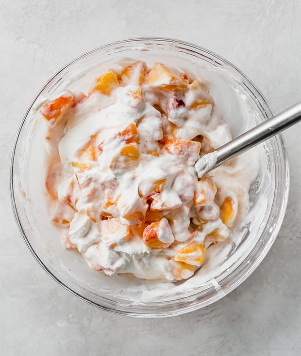 A bowl of chopped peaches mixed with freshly whipped cream.