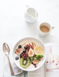 A white bowl with fruits next to a spoon.