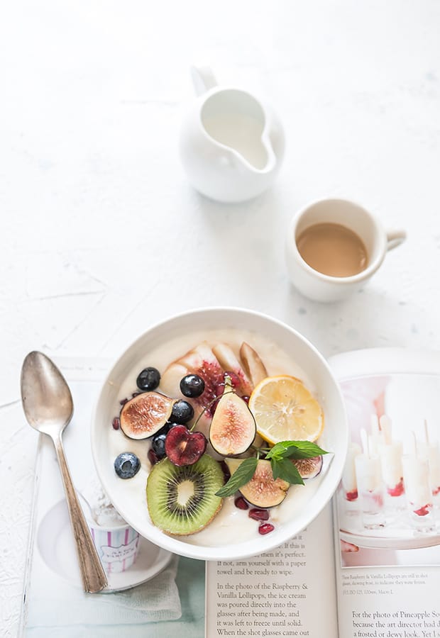 A white bowl with fruits next to a spoon.