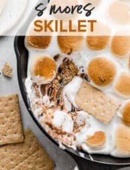 A graham cracker dipping into the melty marshmallows and exposing the melted Reeses peanut butter cup underneath the Reeses Peanut Butter Cup S'mores Skillet.