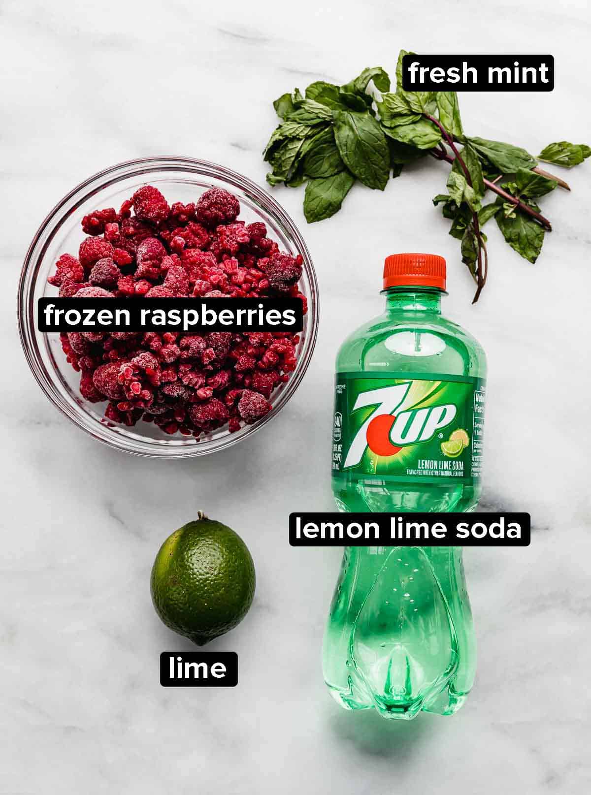 Raspberry Mojito Mocktail ingredients on a white background: raspberries, mint, lime, and lemon lime soda.