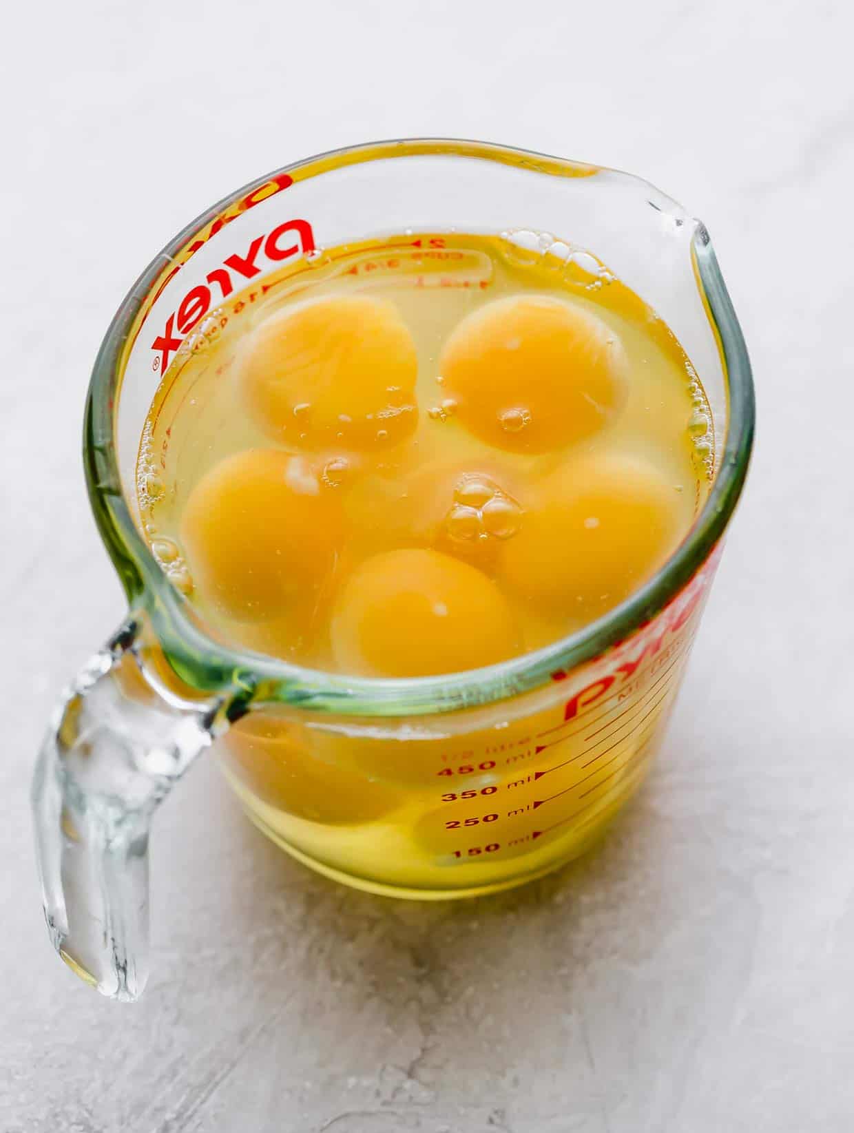 A glass liquid measuring cup with cracked eggs in it.
