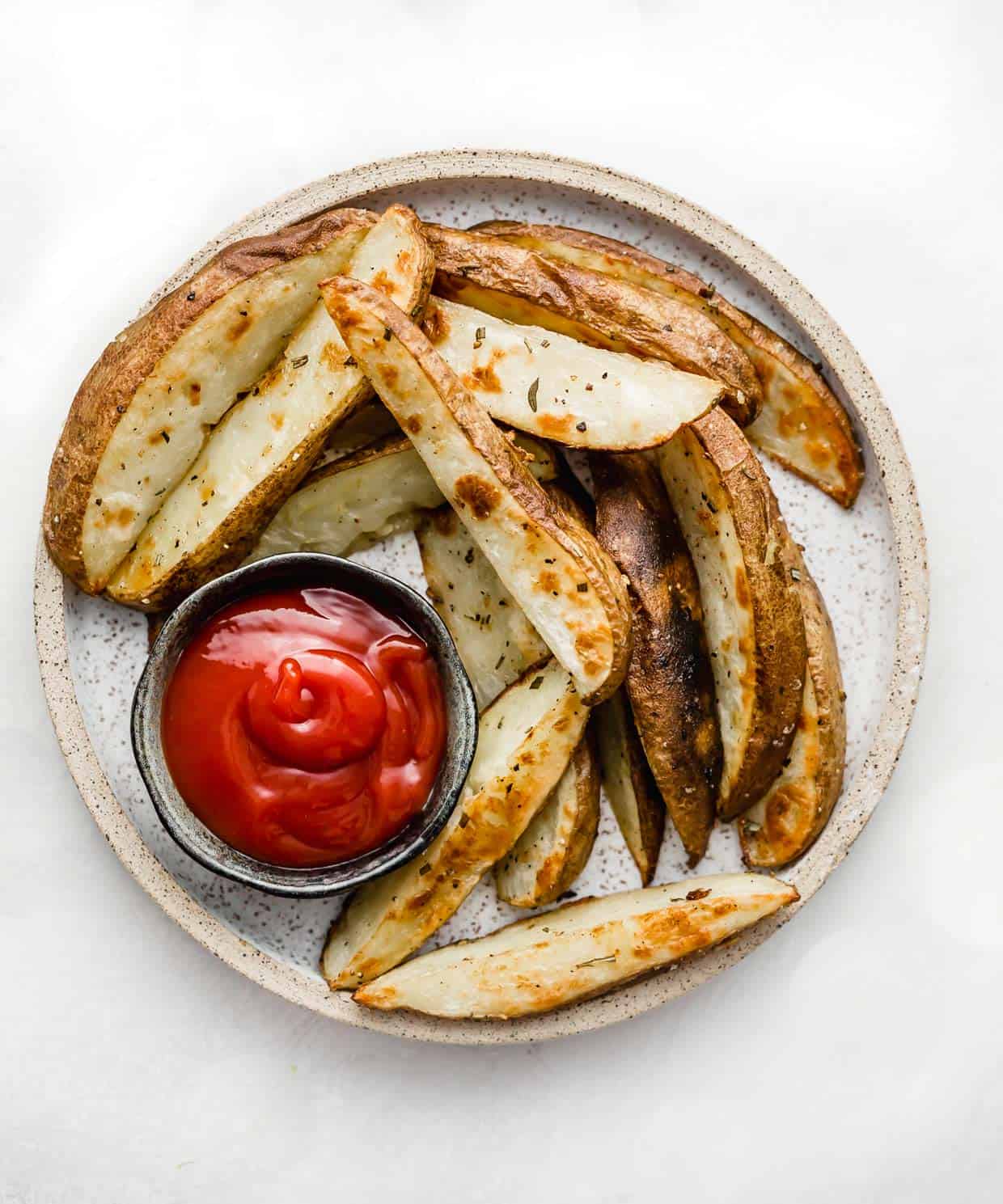 Crispy Baked Potato Wedges on a plate with a black bowl filled with ketchup.