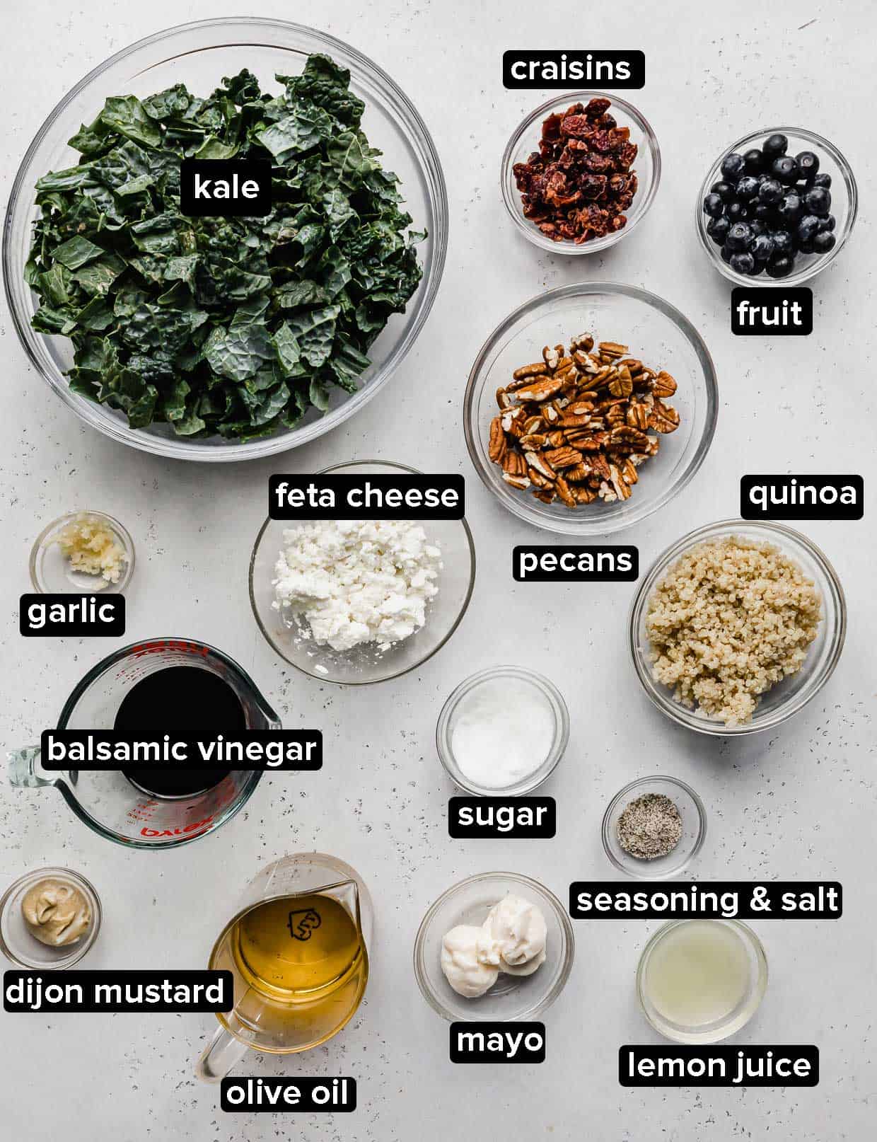 Kale and Quinoa Salad ingredients portioned into glass bowls on a light gray background. 