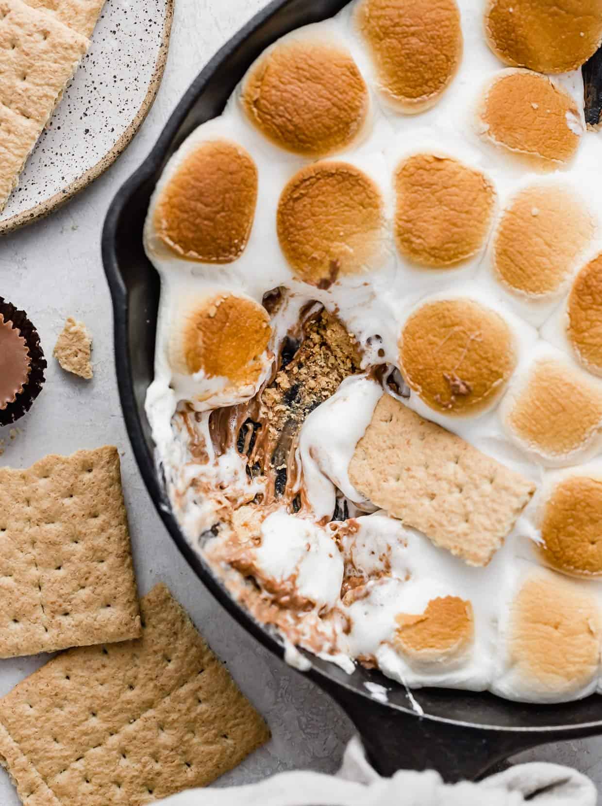 Reese's S'mores in a skillet with a graham cracker scooping into the marshmallows and peanut butter cups.