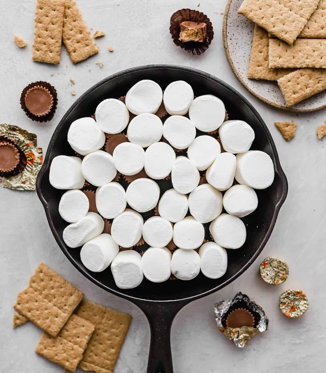 Large marshmallows overtop of Reese's peanut butter cups in a black skillet.