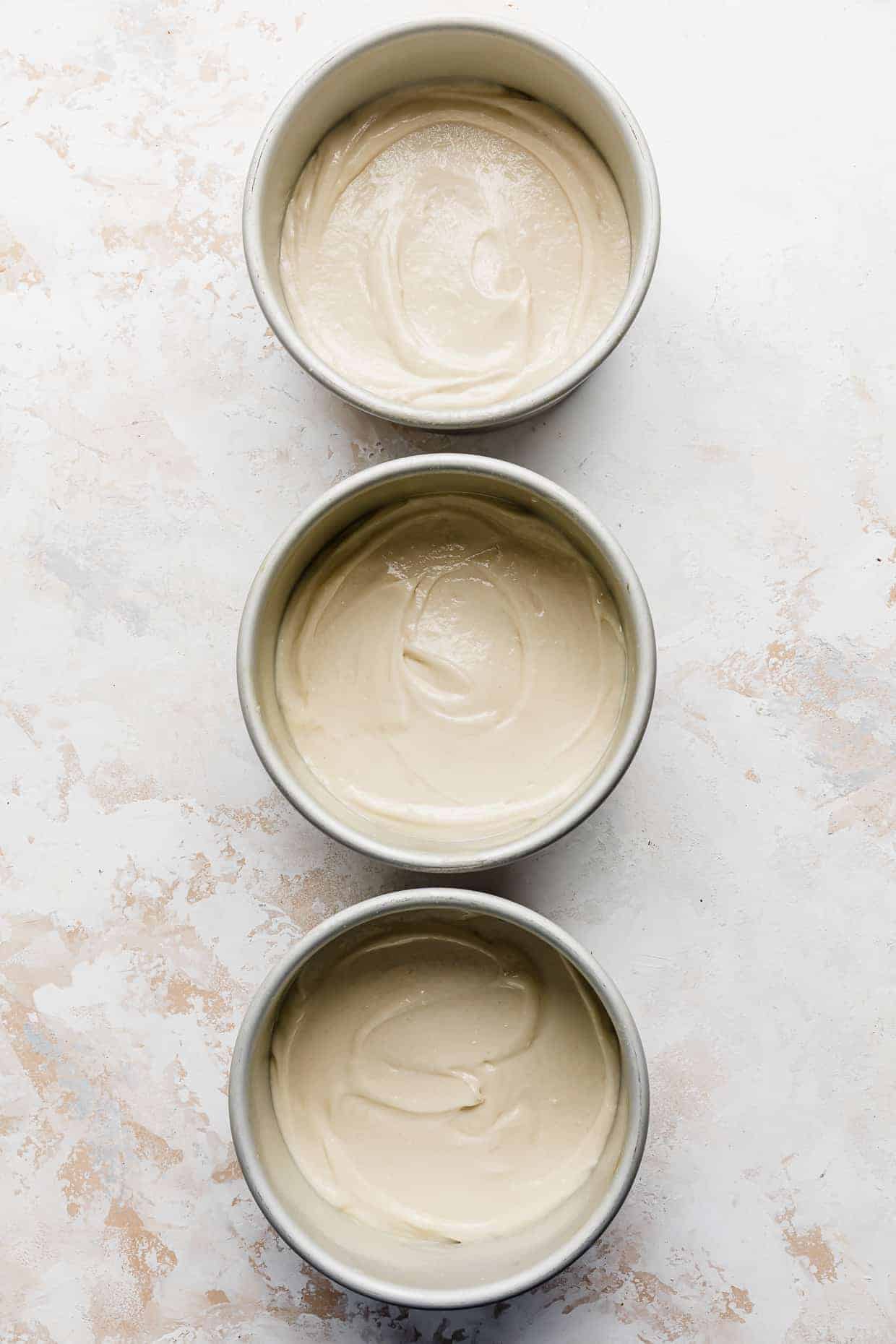 Three circular pans with vanilla cake batter in each.