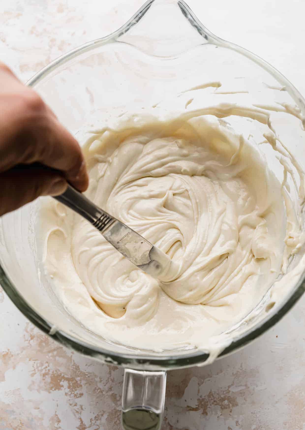 A butter knife running through a bowl full of vanilla cake batter.
