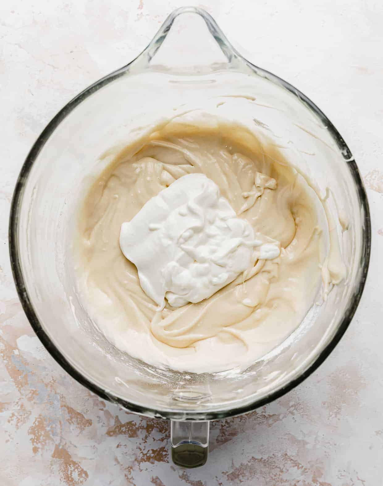 A glob of sour cream atop cake batter in a glass bowl.