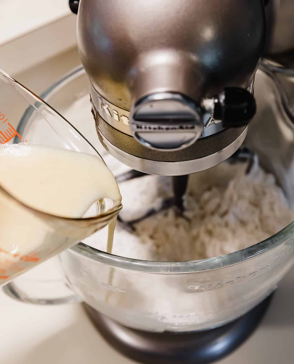 Liquid ingredients being poured into a stand mixer bowl.
