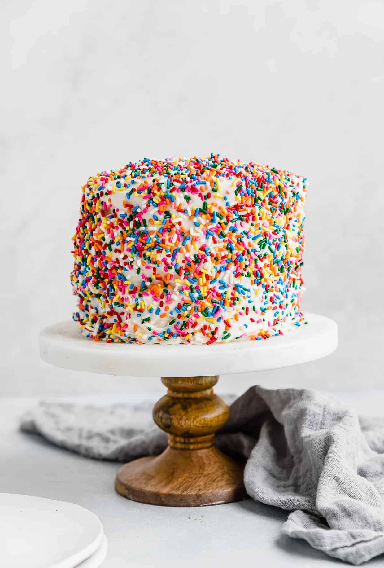 A sprinkle smash cake recipe on a cake stand against a white background.