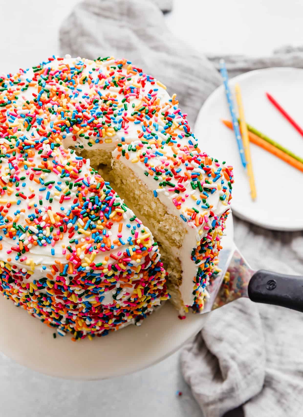 A sprinkle smash cake recipe with a slice of cake cut and being lifted out of the cake.
