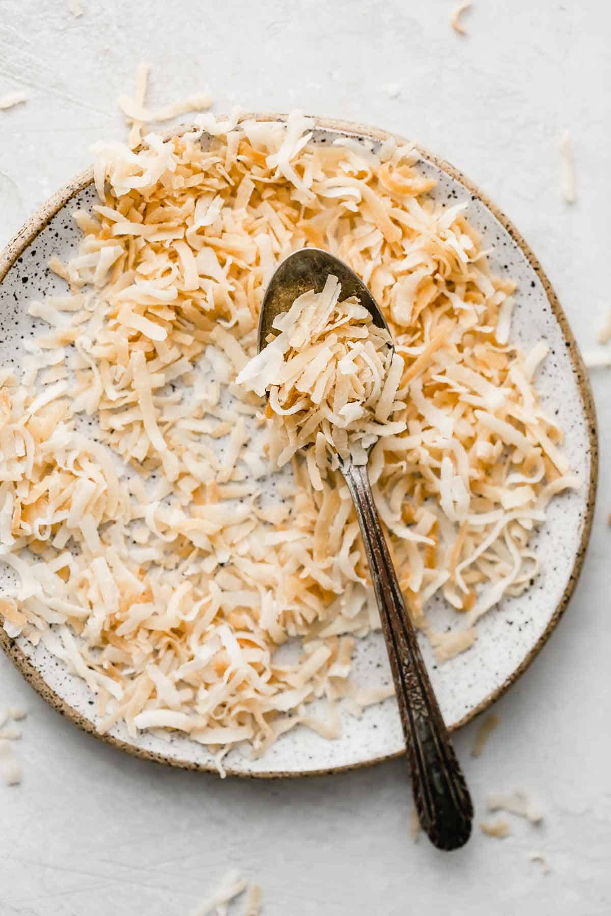 A white plate topped with toasted coconut and a spoon.