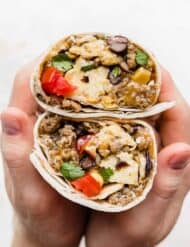 A set of hands holding a Breakfast Burrito with Black Beans that is wrapped in a tortilla and cut in half.