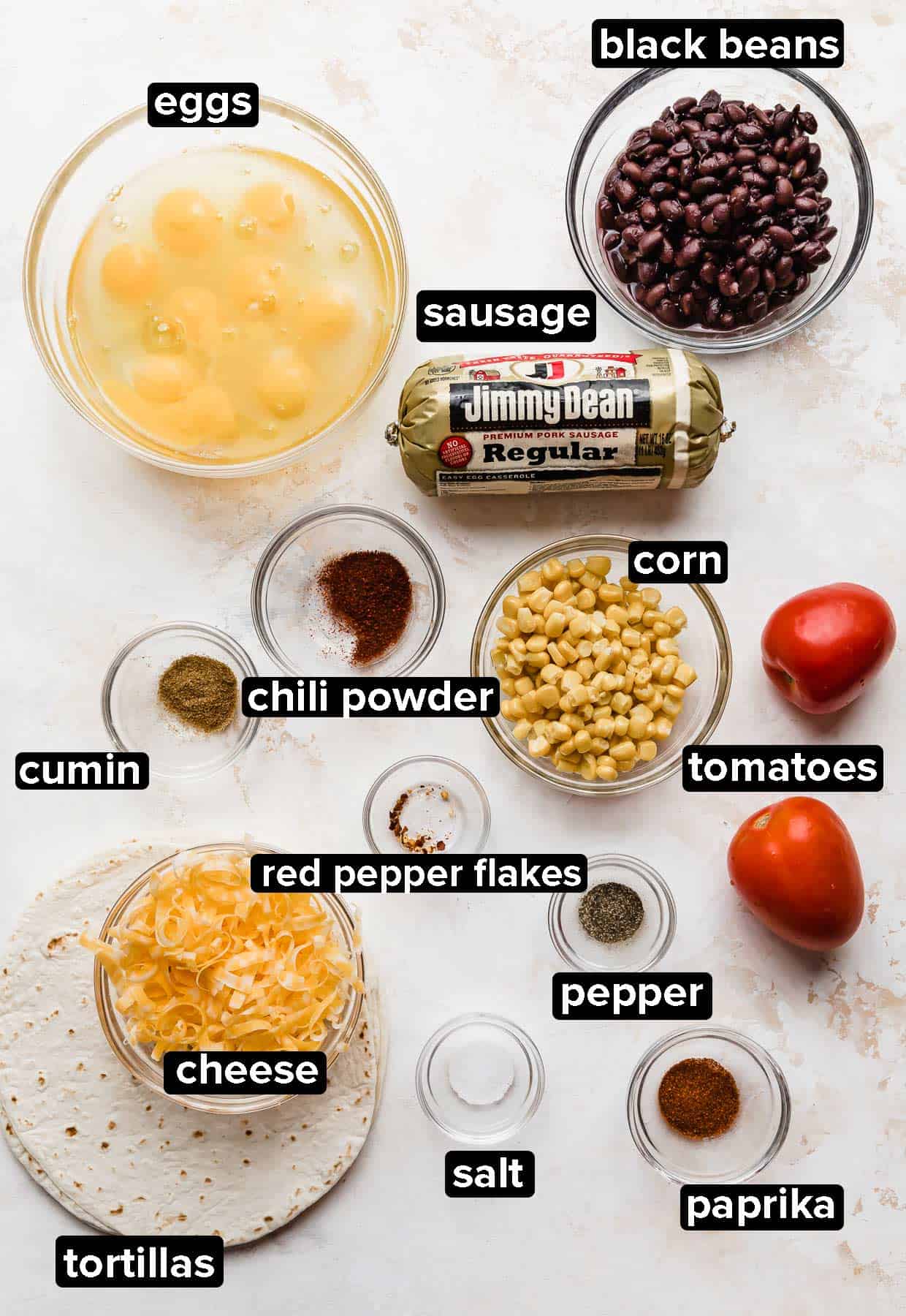 Ingredients used to make Breakfast Burrito with Black Beans and egg and sausage, portioned into glass bowls on a white textured background.