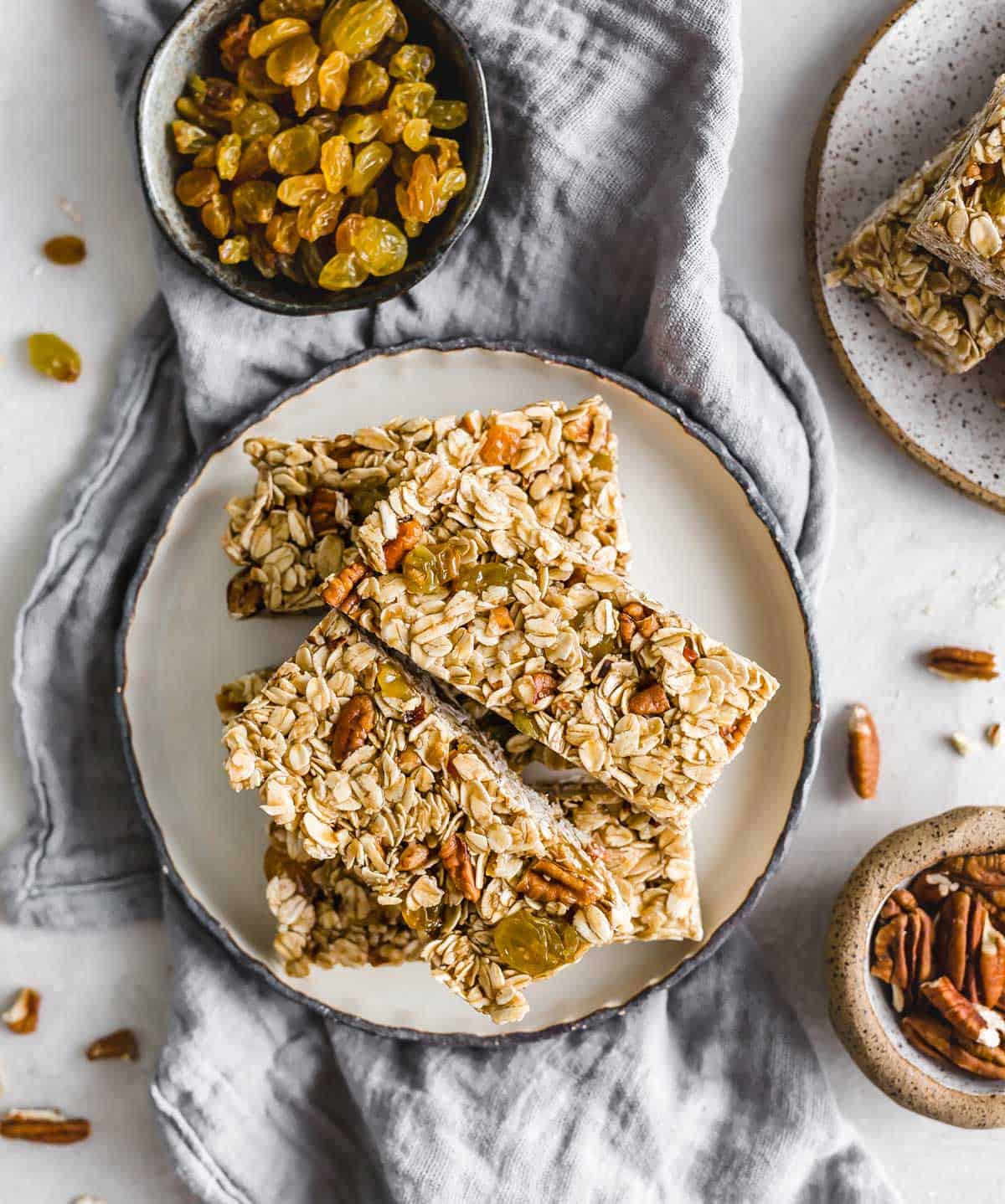 Homemade Oatmeal Raisin Granola Bars with nuts and golden raisins on a black rimmed white plate on a light gray linen napkin.