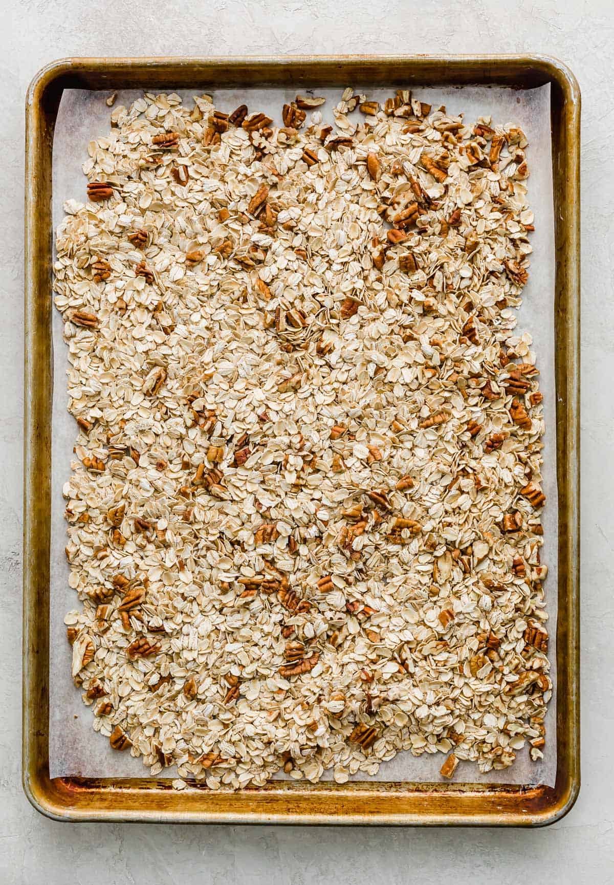 A baking sheet with old fashioned oats and chopped pecans spread across the surface of it.