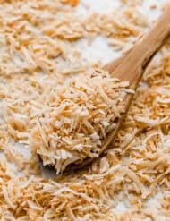 A wooden spoon topped with toasted coconut, demonstrating How to Toast Coconut.