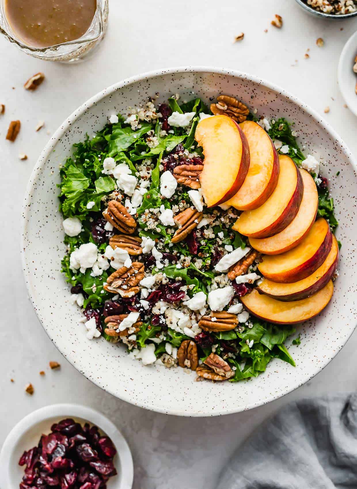 A Kale and Quinoa Salad with Cranberries and Feta and sliced peaches in a white bowl.