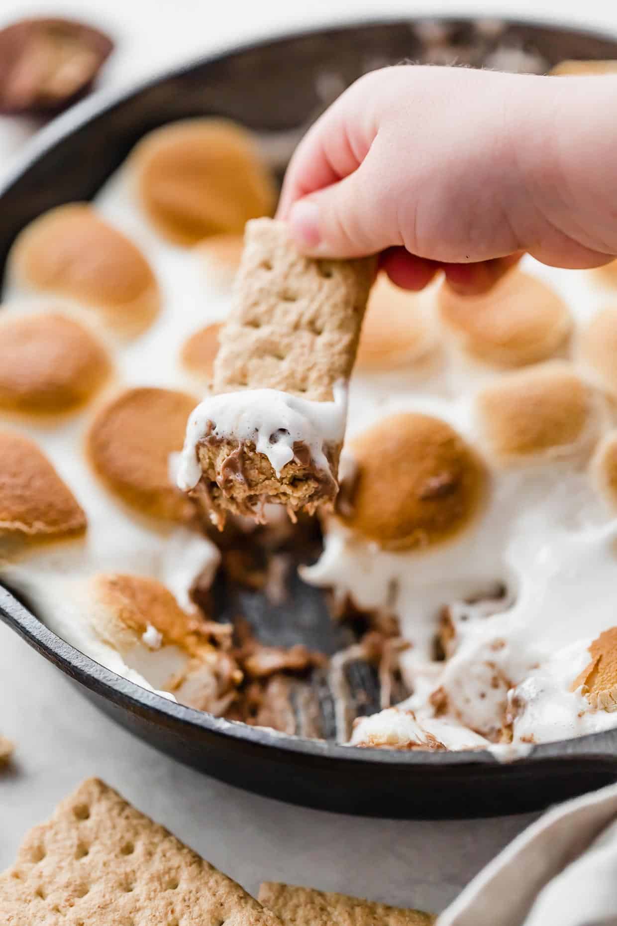 A hand dipping a graham cracker into a Reese's S'mores skillet.
