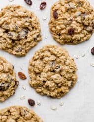 A Soft Oatmeal Raisin Cookie surrounded by oats and raisins.