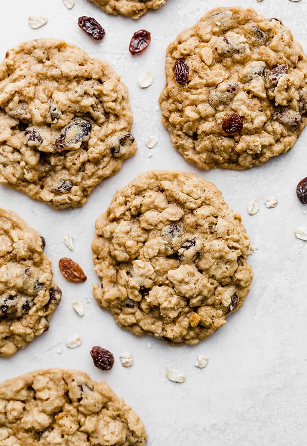 A Soft Oatmeal Raisin Cookie surrounded by oats and raisins.