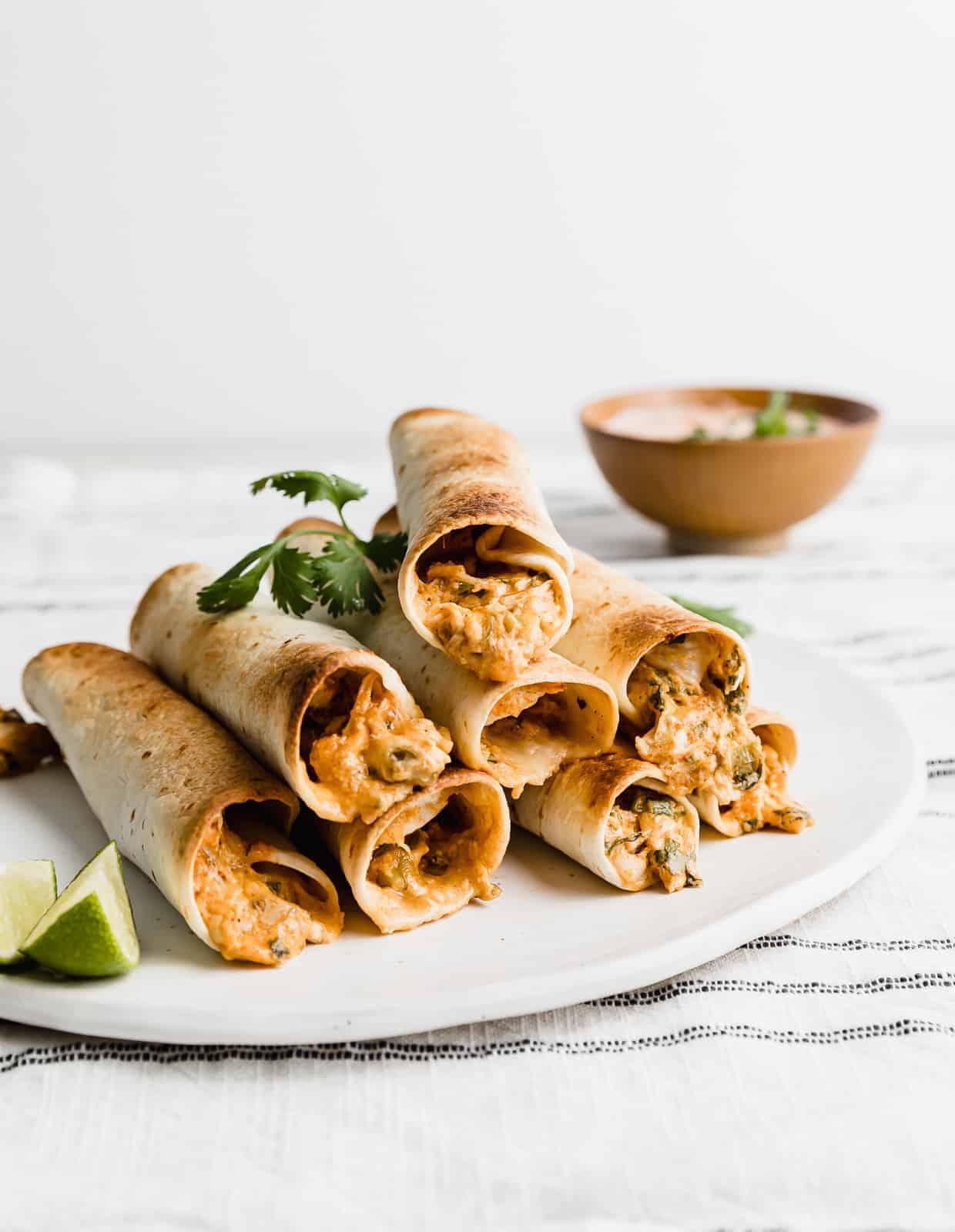 Baked Chicken Taquitos stacked on top of one another on a white plate.