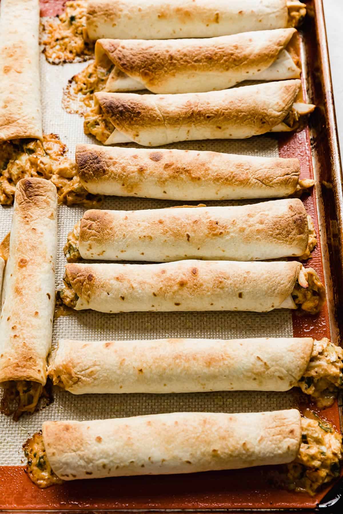 Golden brown baked chicken taquitos lined up on a baking sheet.