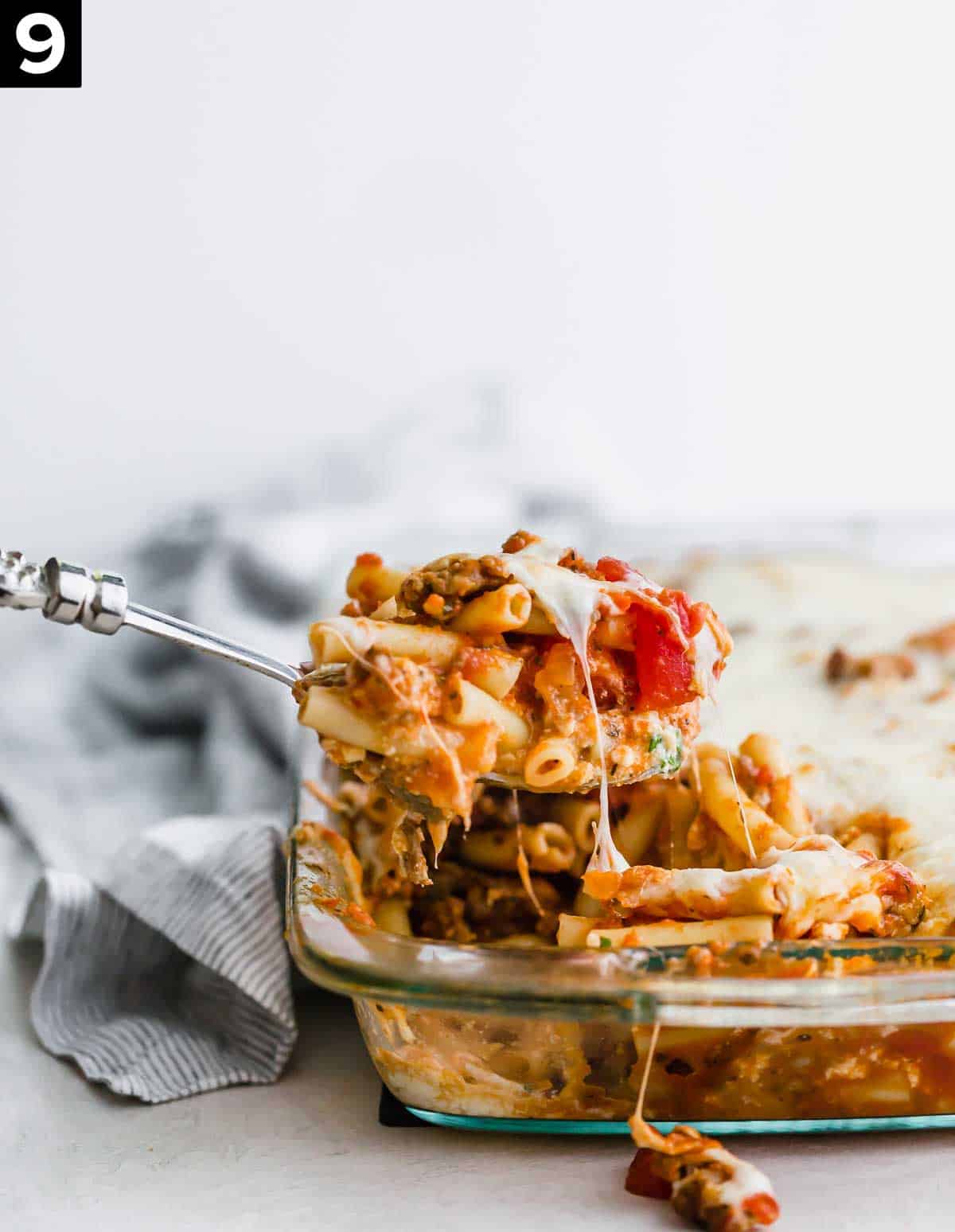 A spoon scooping up baked ziti from a casserole dish.