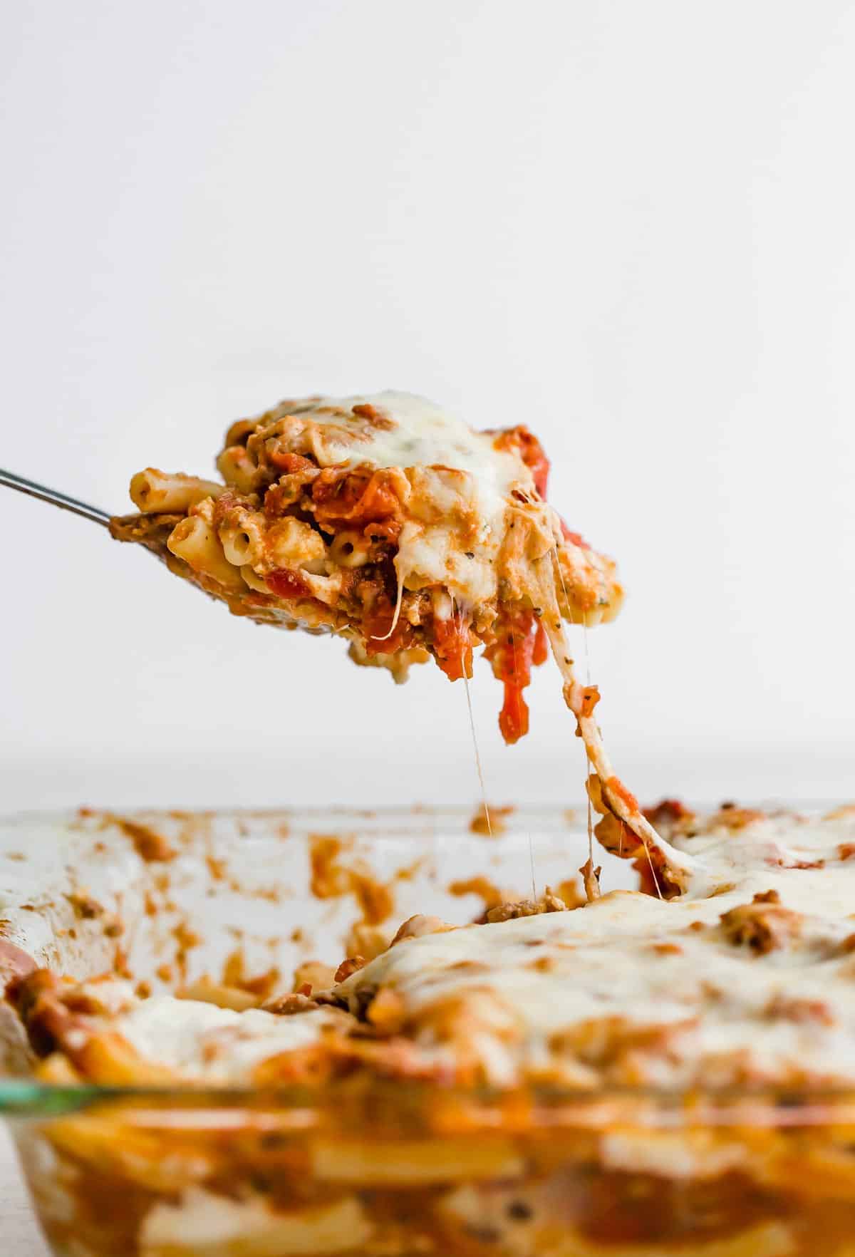 A serving spoon scooping up cheesy baked ziti.