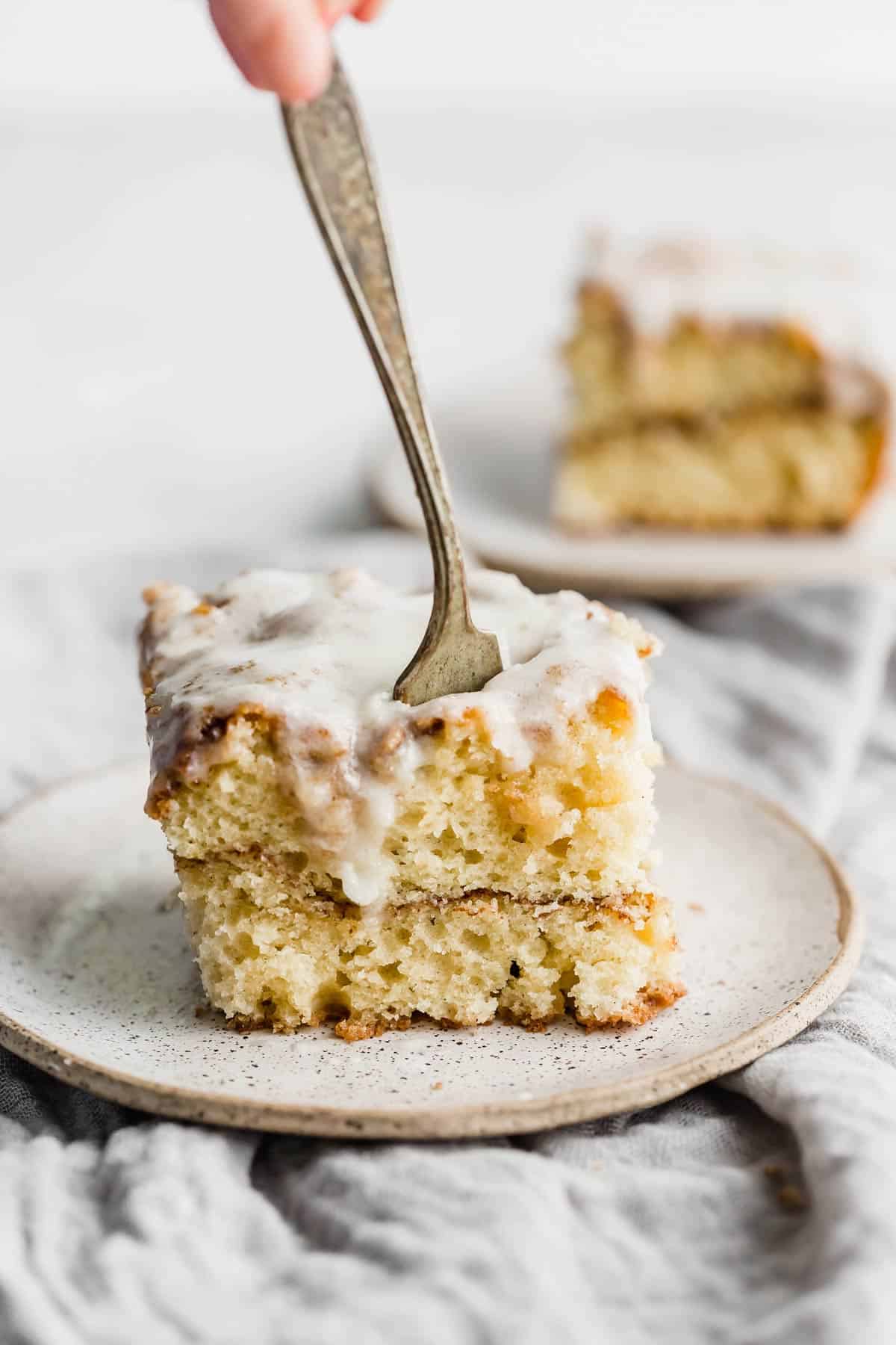 A fork cutting into an easy cinnamon roll cake slice on a white plate.
