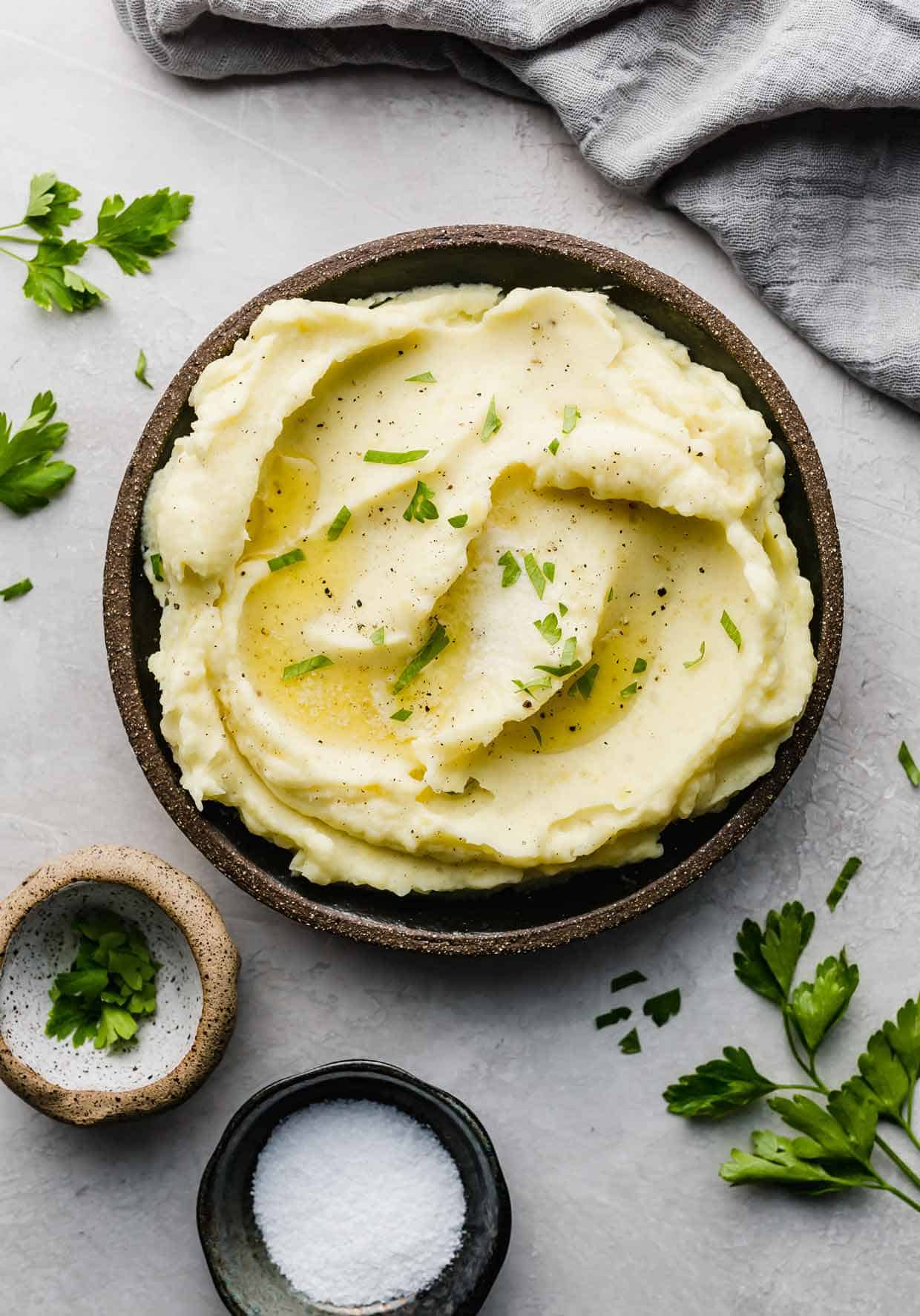 Swirled homemade mashed potatoes on a black plate topped with fresh chopped parsley.
