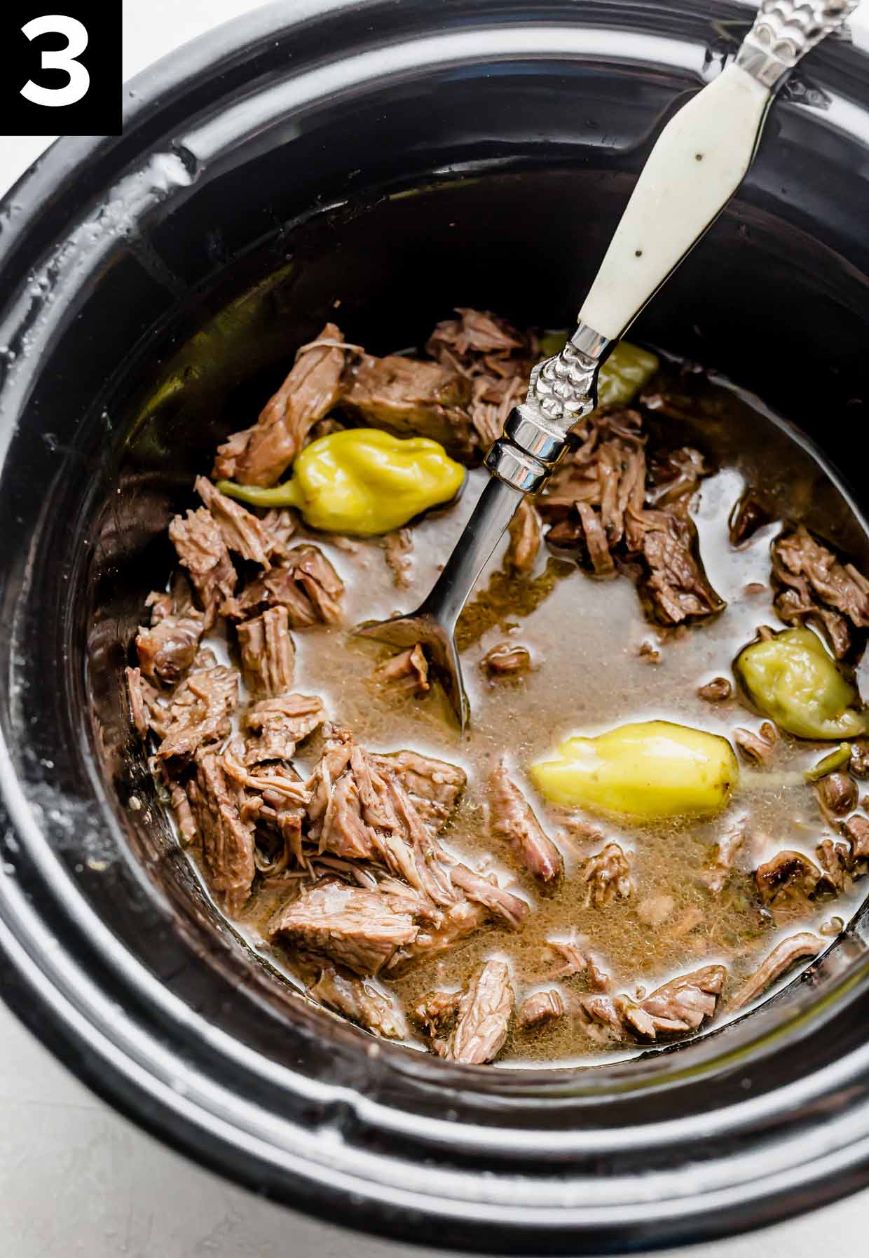 Crock pot Mississippi Pot Roast in a black slow cooker with pepperoncini peppers amongst the meat.
