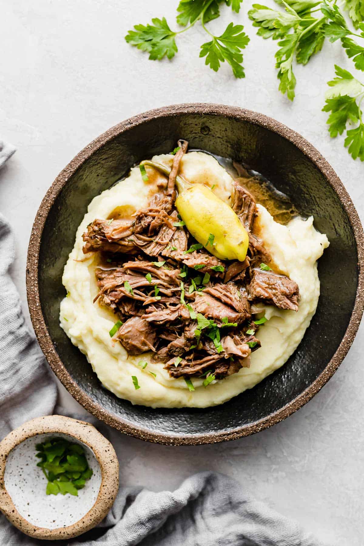 Mississippi Pot Roast overtop white mashed potatoes on a black plate.