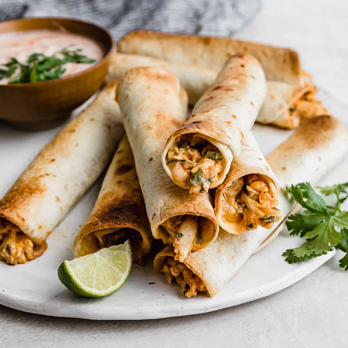 Baked Chicken Taquitos stacked on top of one another on a white plate with fresh parsley in the background.