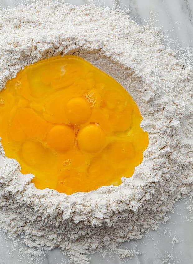 Eggs and egg yolks filling a flour mound.